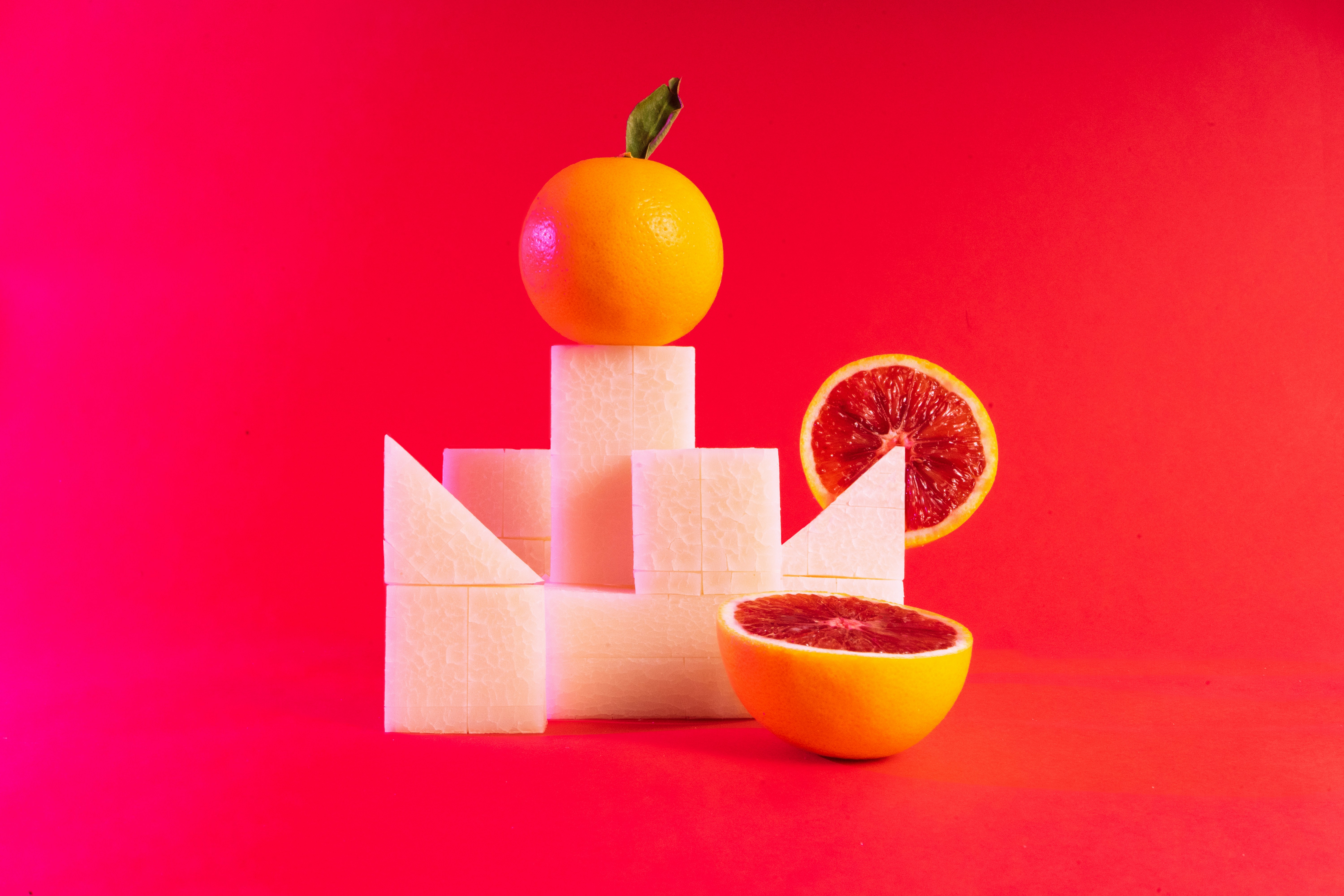 Citrus fruit arranged with geometric blocks against a red backdrop